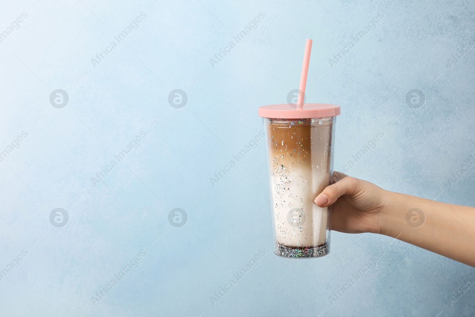 Photo of Woman holding glass of caramel macchiato on color background, closeup. Space for text