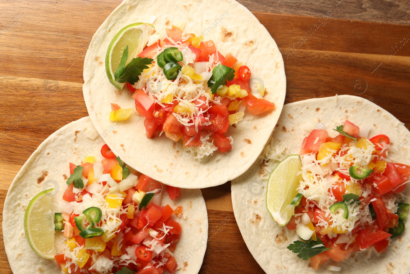 Photo of Delicious tacos with vegetables and lime on wooden table, top view