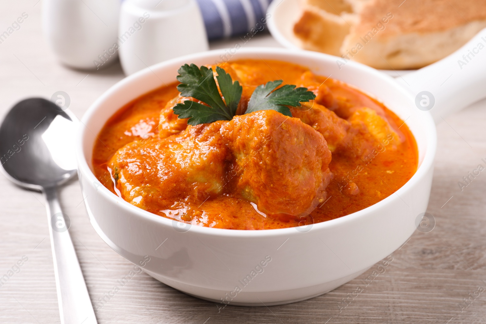 Photo of Bowl of delicious chicken curry on white wooden table