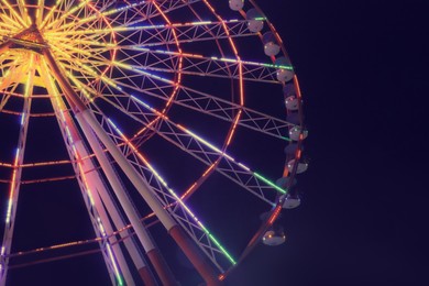 Photo of Beautiful glowing Ferris wheel against dark sky, low angle view. Space for text