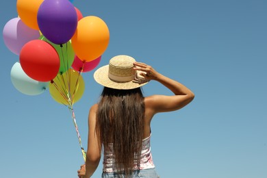 Woman with bunch of colorful balloons against blue sky, back view