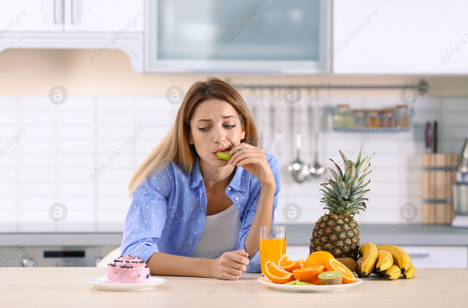 Photo of Woman choosing between dessert and fruits at table in kitchen. Healthy diet