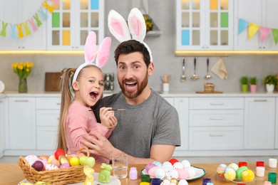 Photo of Emotional father with his cute daughter and Easter eggs at table in kitchen