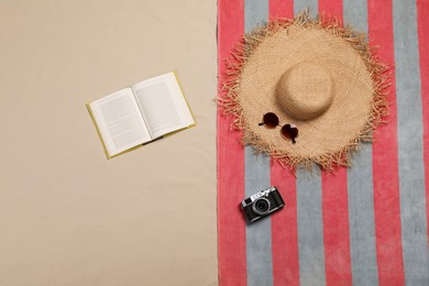 Photo of Beach towel, hat, sunglasses, camera and open book on sand, flat lay