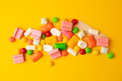 Photo of Many different chewing gums on yellow background, flat lay