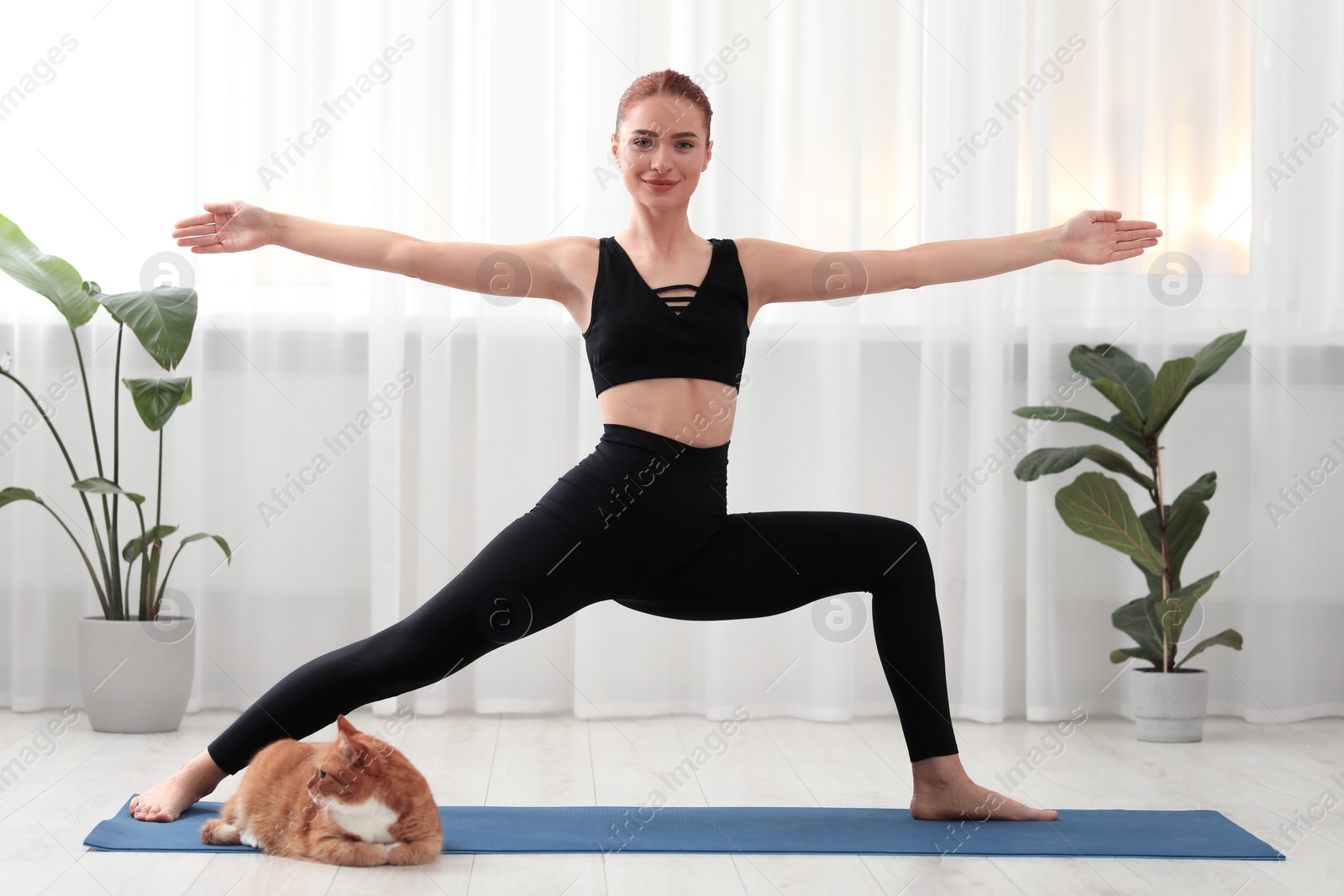 Photo of Beautiful woman with cute red cat practicing yoga on mat at home