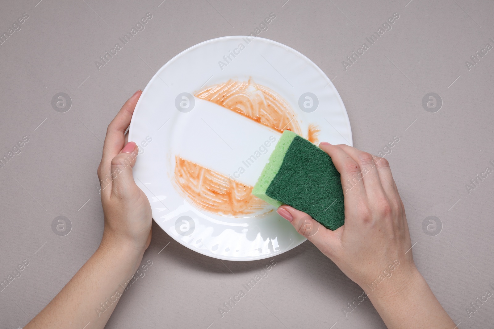 Photo of Woman washing dirty plate with sponge on grey background, top view