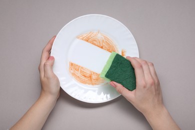 Woman washing dirty plate with sponge on grey background, top view