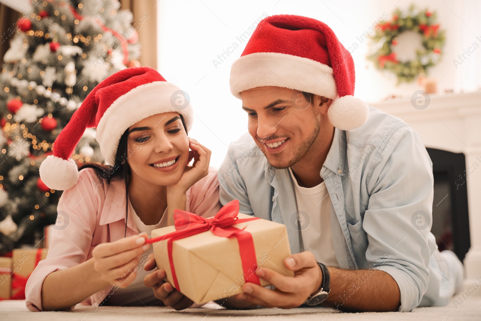 Photo of Happy couple in Santa hats with Christmas gift at home