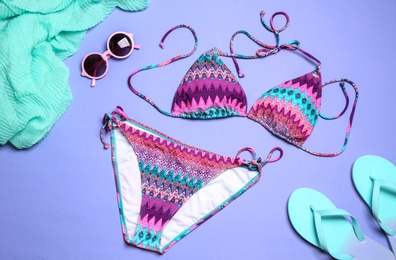 Stylish bright bikini and beach accessories on color background, above view