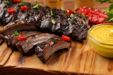 Photo of Tasty grilled ribs and sauce on wooden table, closeup