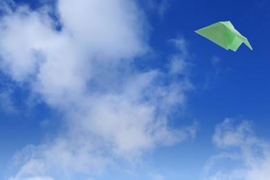 Image of Green paper plane flying in blue sky with clouds