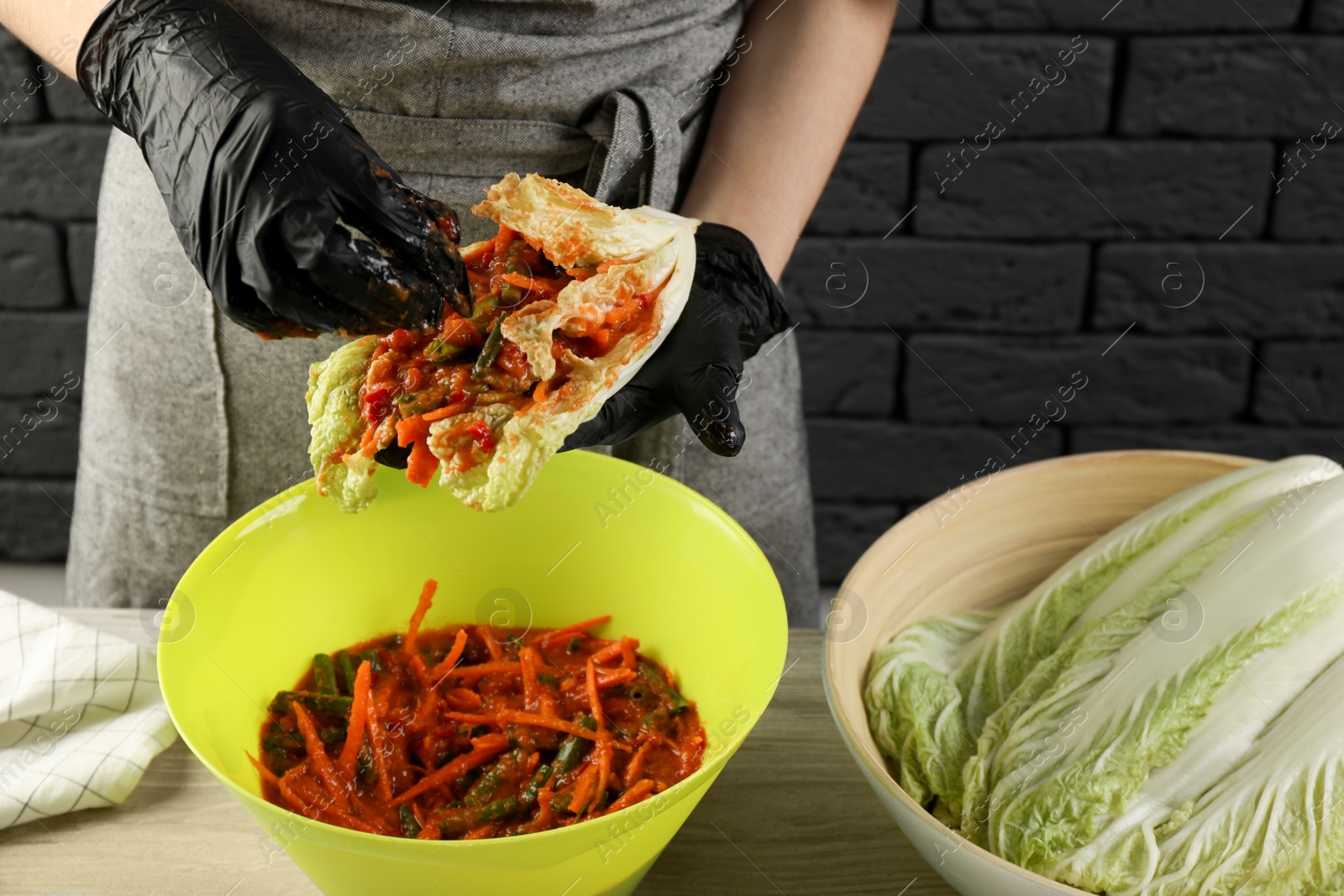 Photo of Woman preparing spicy cabbage kimchi at wooden table indoors, closeup