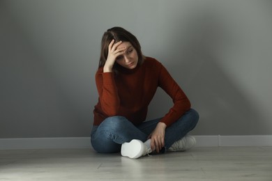 Photo of Sad young woman sitting on floor near grey wall indoors