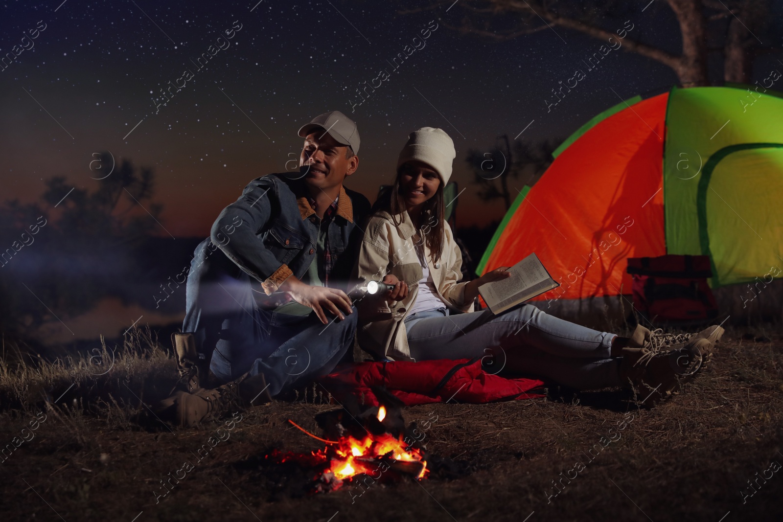 Photo of Couple with flashlight near bonfire at night. Camping season