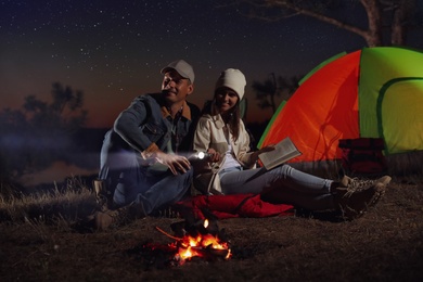 Couple with flashlight near bonfire at night. Camping season
