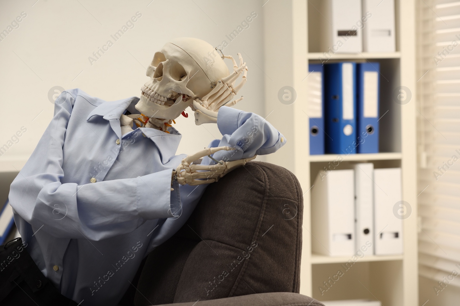 Photo of Waiting concept. Human skeleton sitting in armchair at office