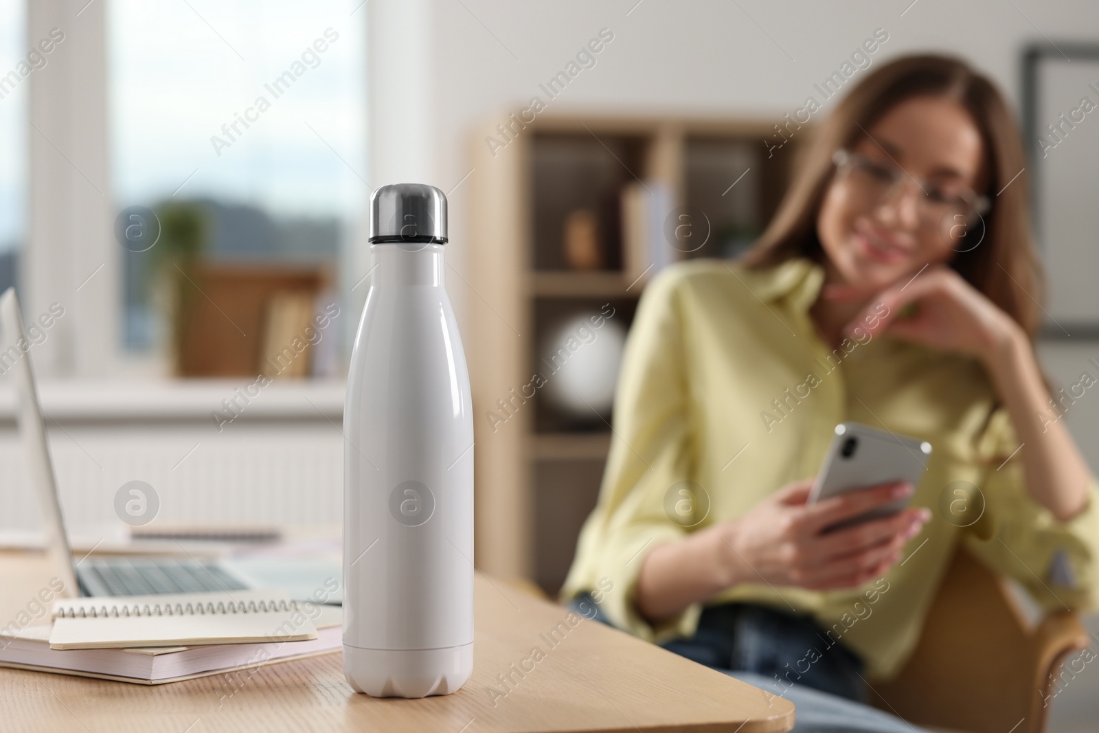 Photo of Woman using smartphone at workplace, focus on thermos bottle. Space for text