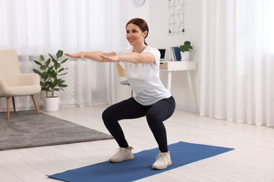 Photo of Morning exercise. Happy woman squatting at home