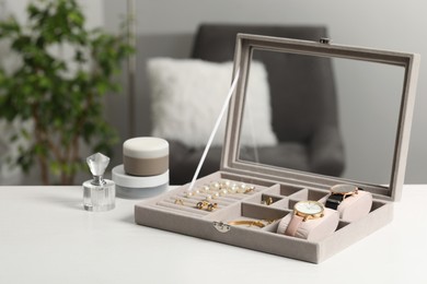 Photo of Jewelry box with many different accessories and perfume on white wooden table indoors