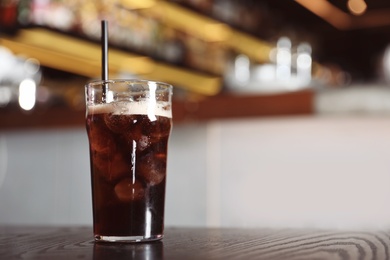 Glass with cola and ice cubes on table indoors. Space for text