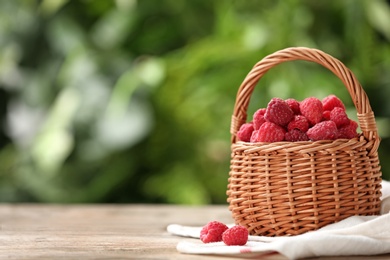 Photo of Wicker basket with delicious ripe raspberries on wooden table against blurred background, space for text