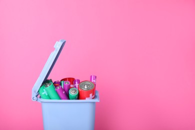 Photo of Many used batteries in recycling bin on pink background. Space for text