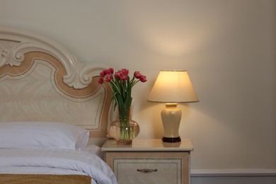 Photo of Comfortable bed and beautiful bouquet on bedside table in room. Stylish interior