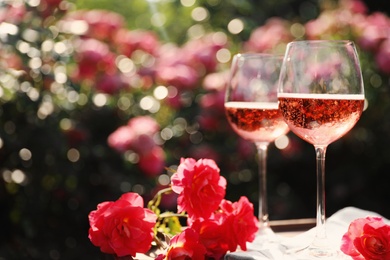 Photo of Glasses of rose wine on table in blooming garden, space for text