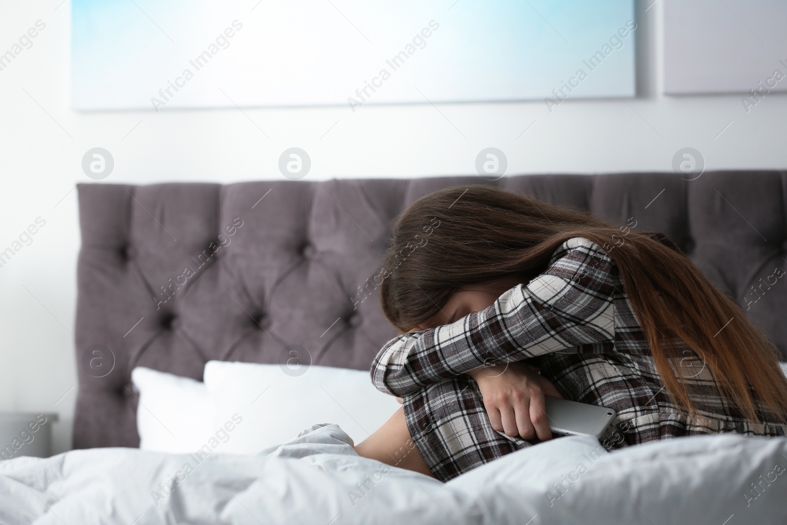 Photo of Upset teenage girl with smartphone sitting on bed. Space for text