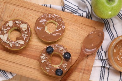 Photo of Slices of fresh apple with nut butter, blueberries and peanuts on table, flat lay