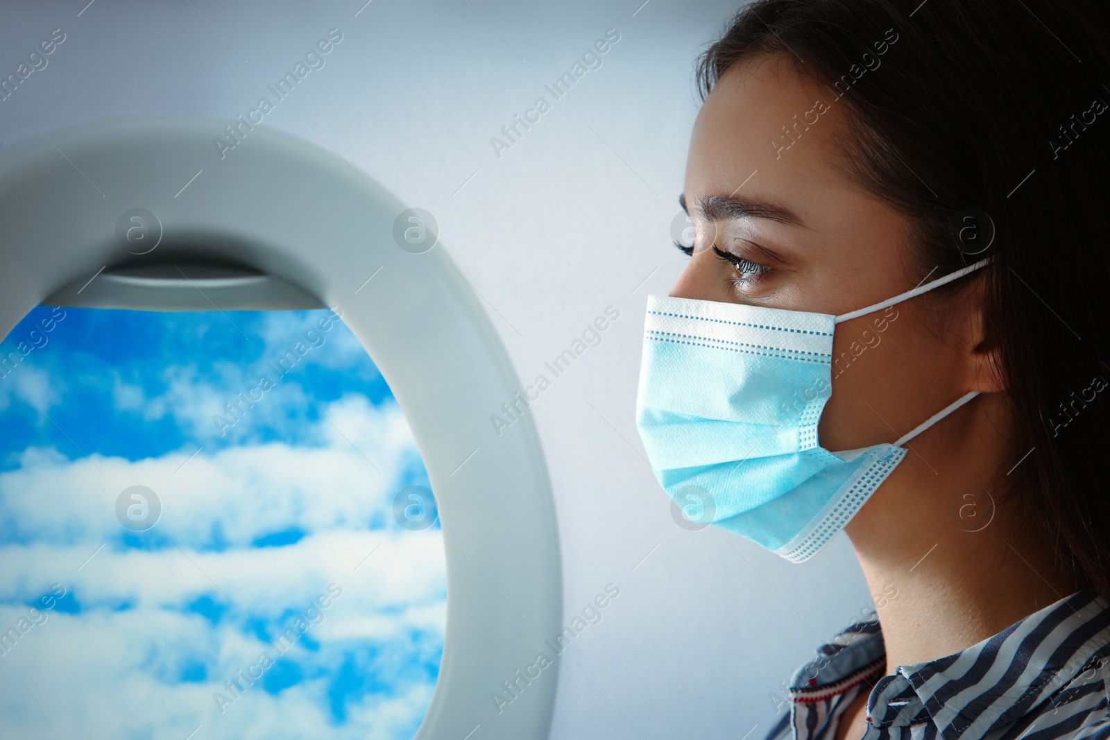 Image of Traveling by airplane during coronavirus pandemic. Woman with face mask near porthole