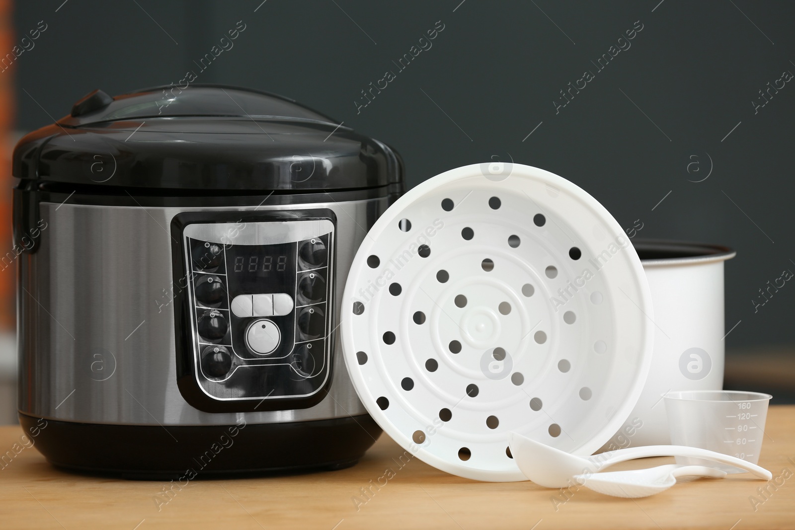 Photo of Modern electric multi cooker, parts and accessories on table against dark background