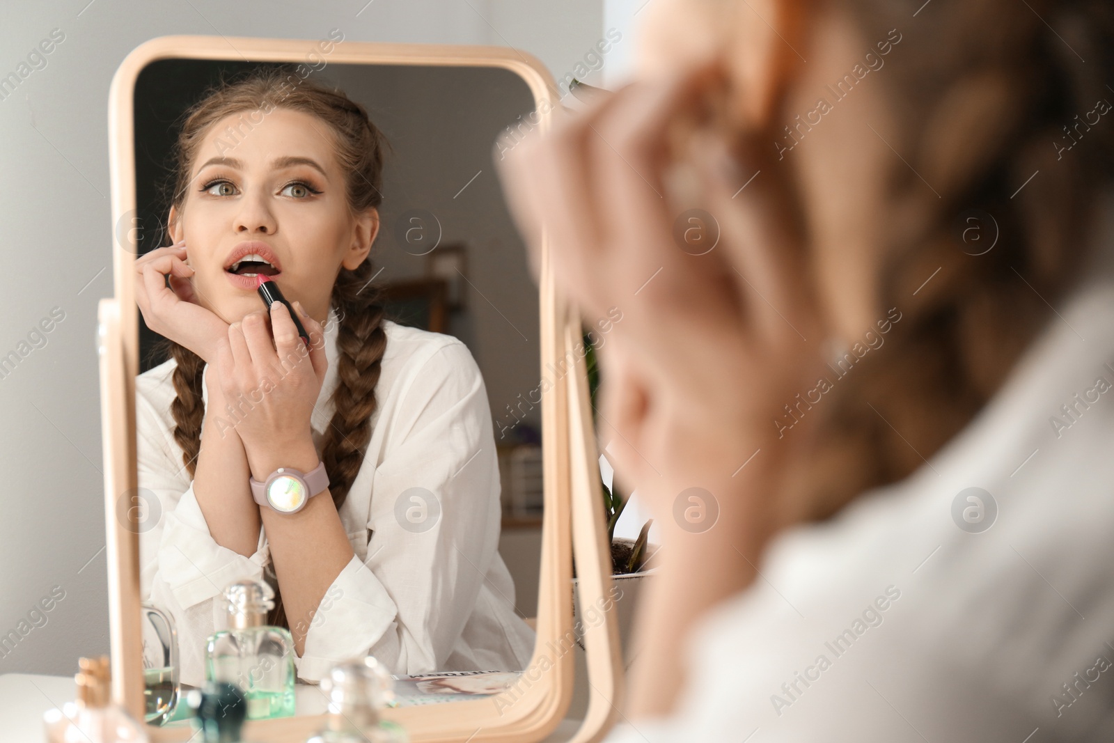 Photo of Portrait of beautiful woman applying makeup near mirror indoors