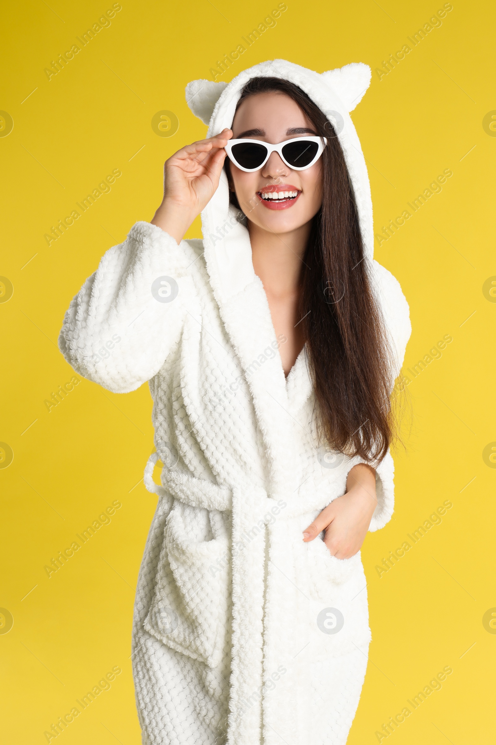 Photo of Young woman in bathrobe and sunglasses on yellow background