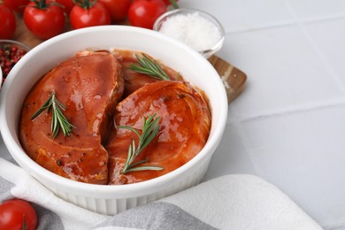 Photo of Raw marinated meat and rosemary in bowl on white tiled table, closeup. Space for text