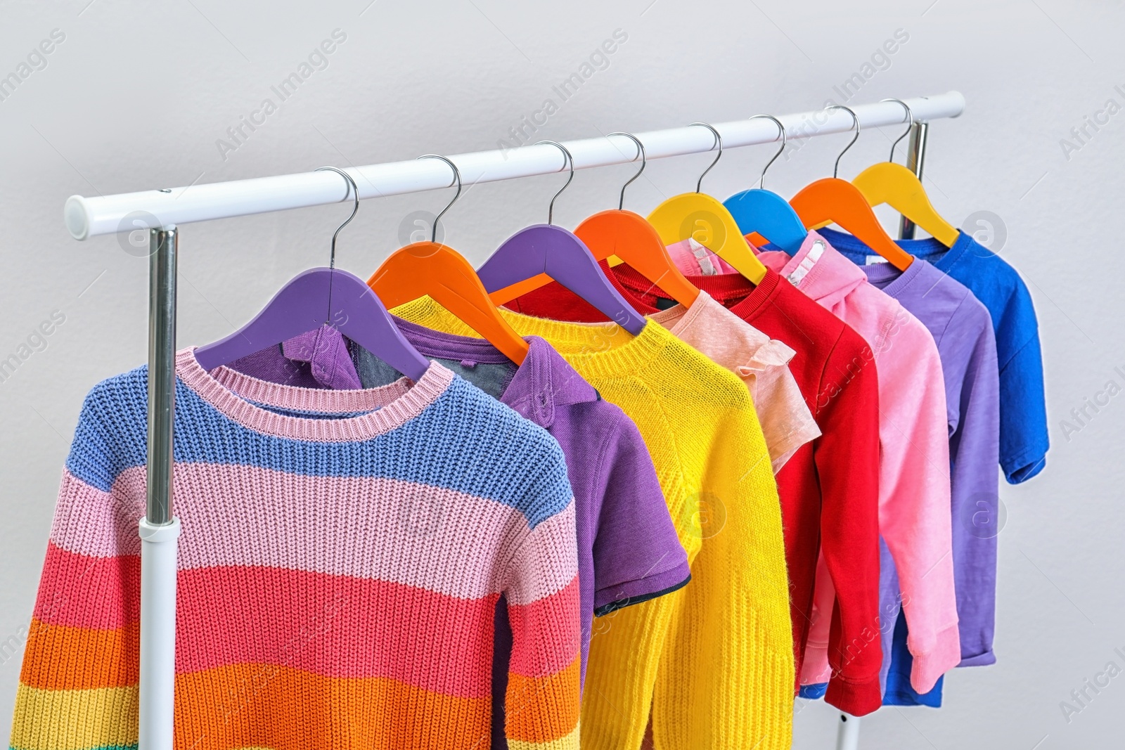 Photo of Colorful clothes hanging on wardrobe rack against light background