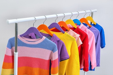 Photo of Colorful clothes hanging on wardrobe rack against light background