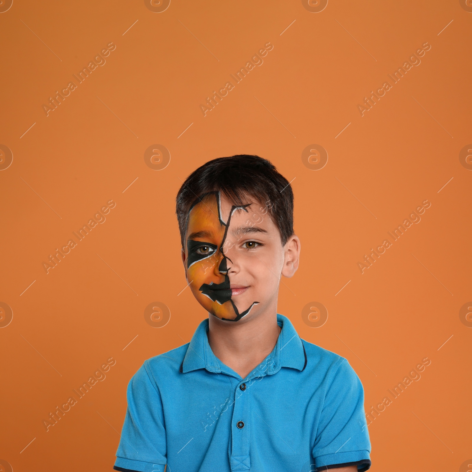 Photo of Cute little boy with face painting on orange background