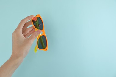 Photo of Woman holding stylish sunglasses on light blue background, closeup. Space for text