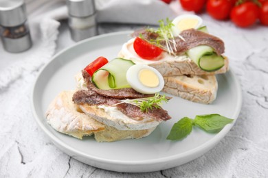 Photo of Delicious bruschettas with anchovies, tomato, cucumber, egg and cream cheese on white textured table