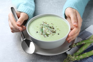 Photo of Woman eating delicious asparagus soup at light grey table, closeup