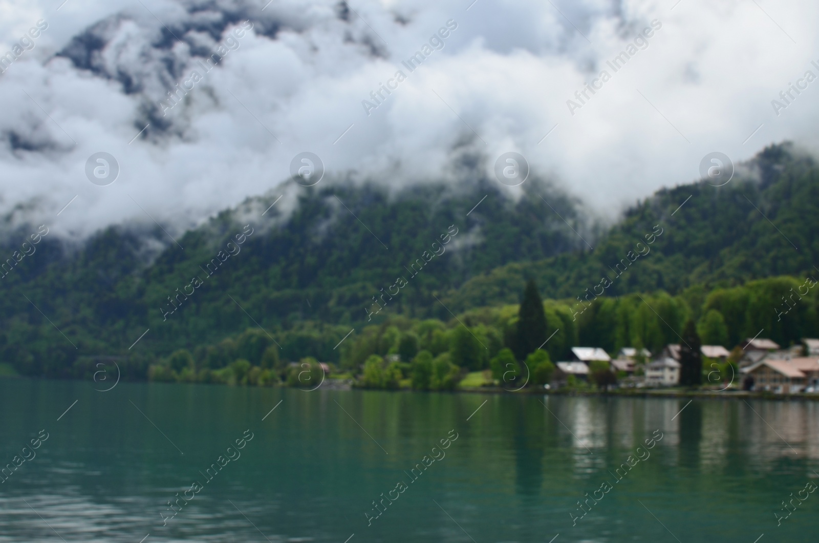 Photo of Blurred view of beautiful village on lake shore near mountains