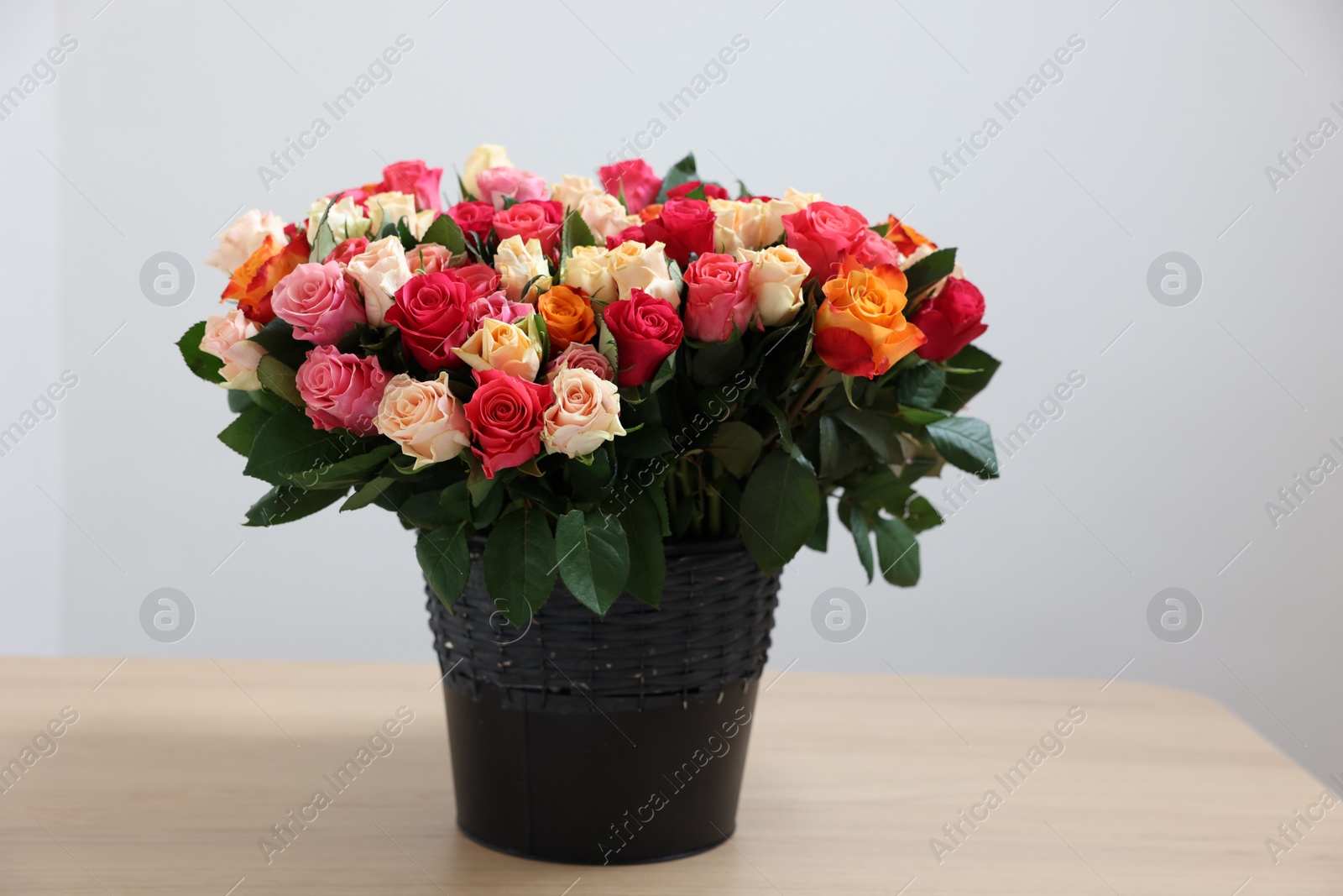 Photo of Bouquet of beautiful roses on wooden table against light background