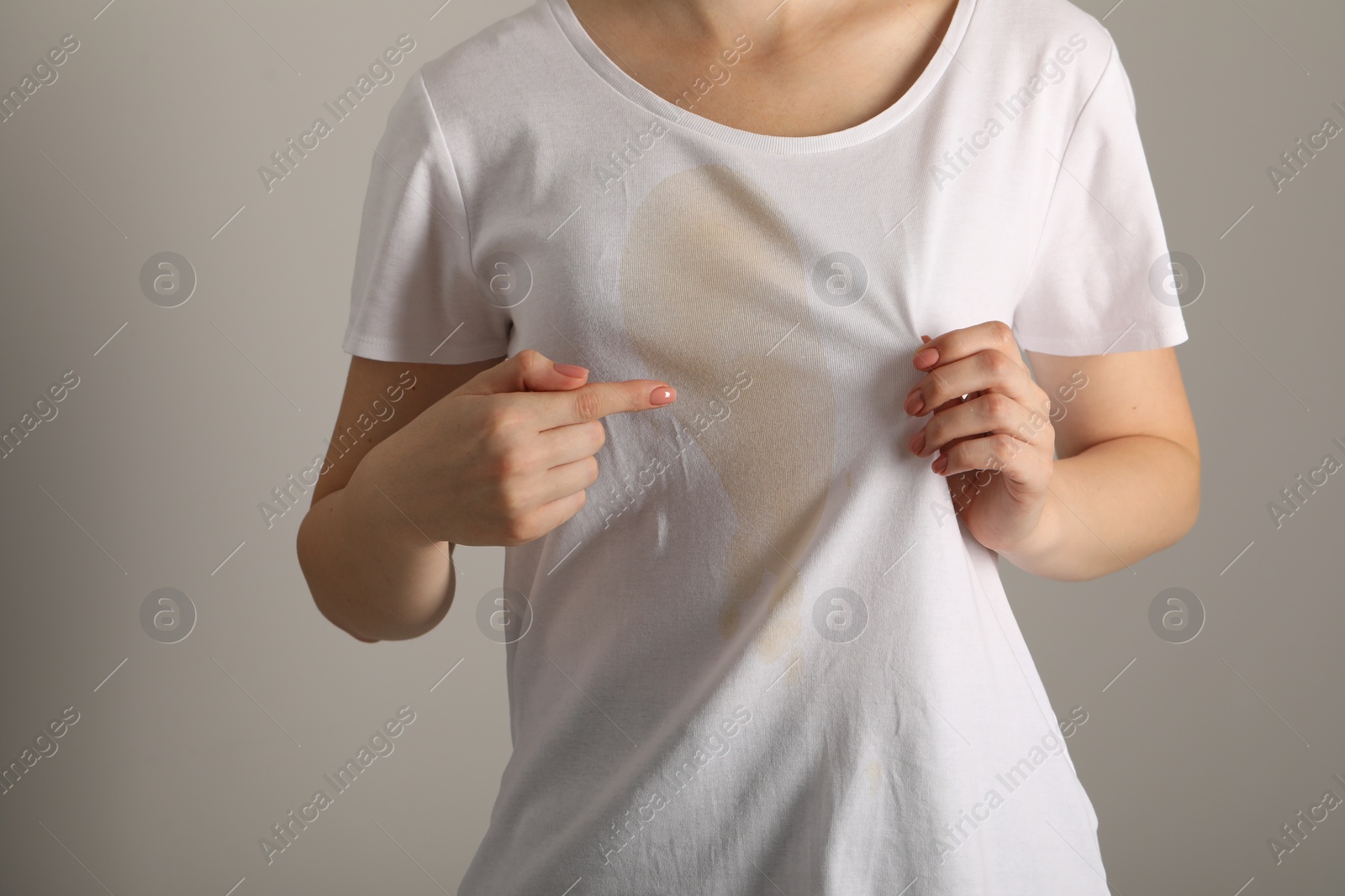 Photo of Woman showing stain from coffee on her shirt against light grey background, closeup