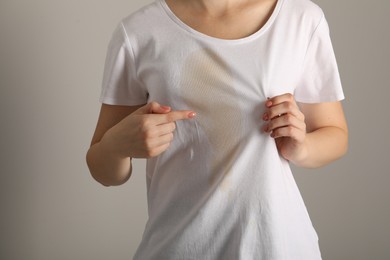 Photo of Woman showing stain from coffee on her shirt against light grey background, closeup