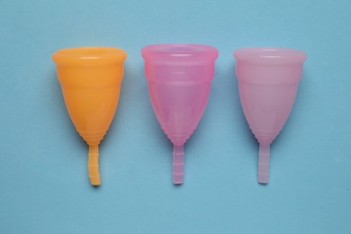 Photo of Different menstrual cups on light blue background, flat lay. Reusable female hygiene product