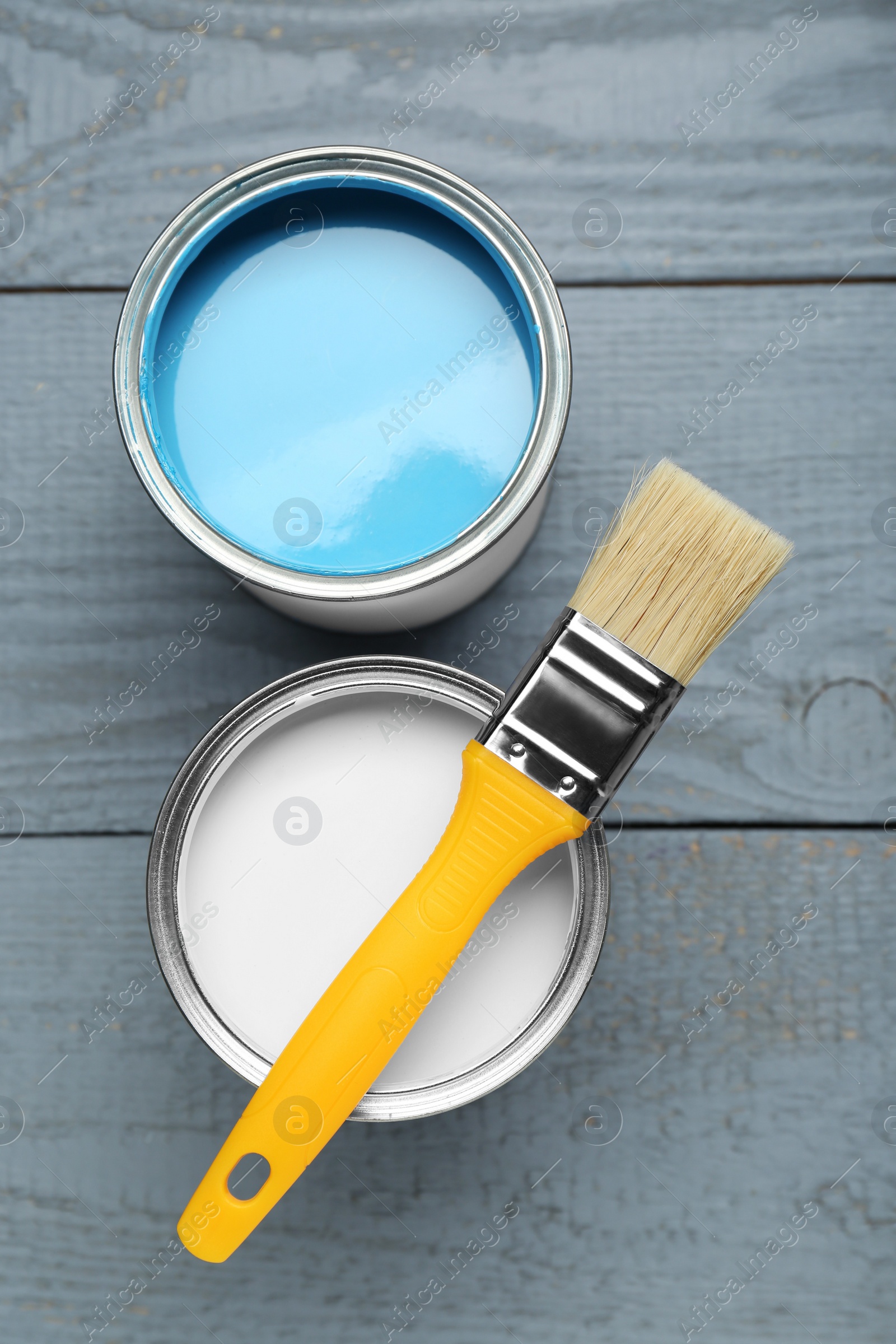 Photo of Cans of colorful paints and brush on grey wooden table, flat lay
