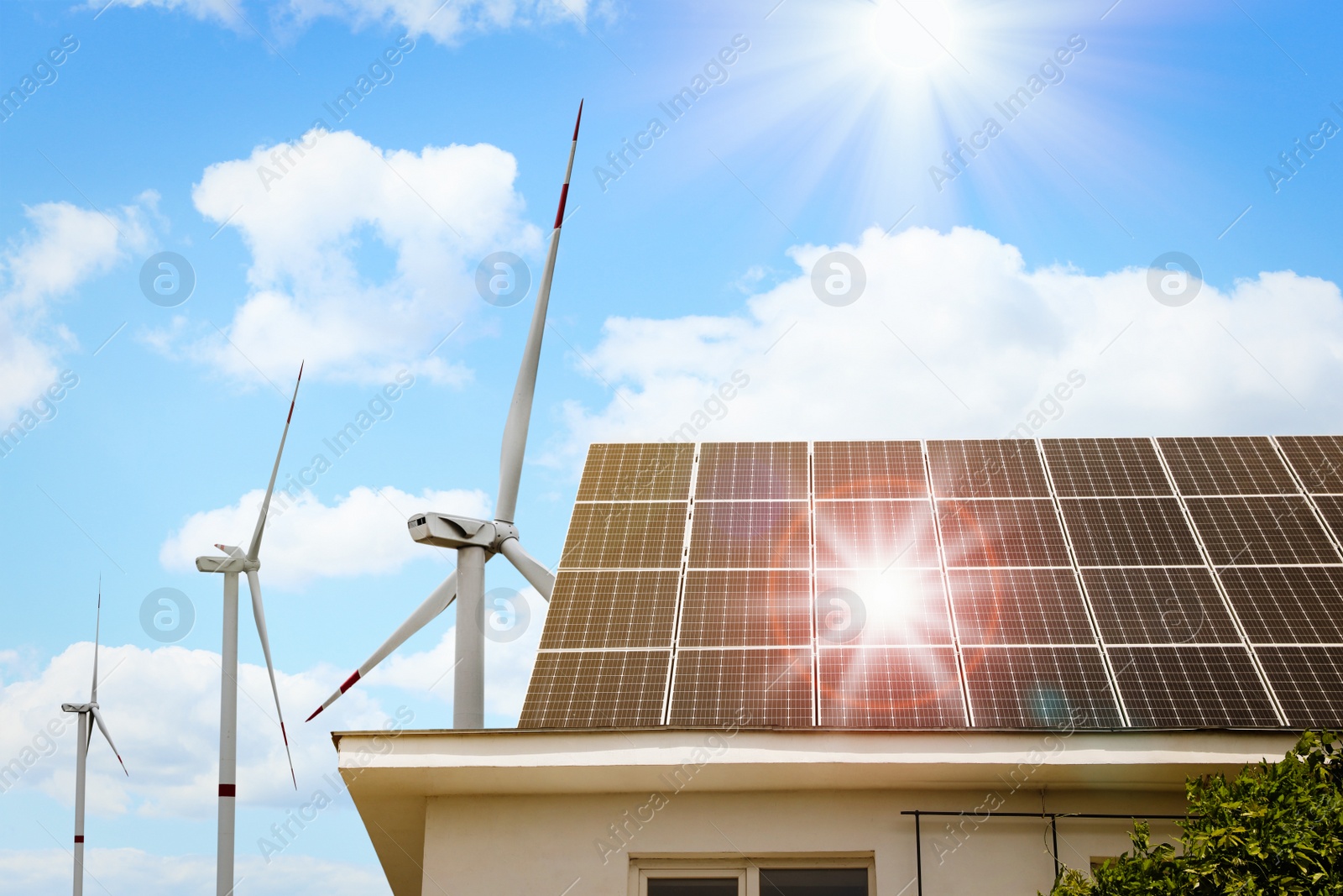 Image of Wind turbines near house with installed solar panels on roof. Alternative energy source