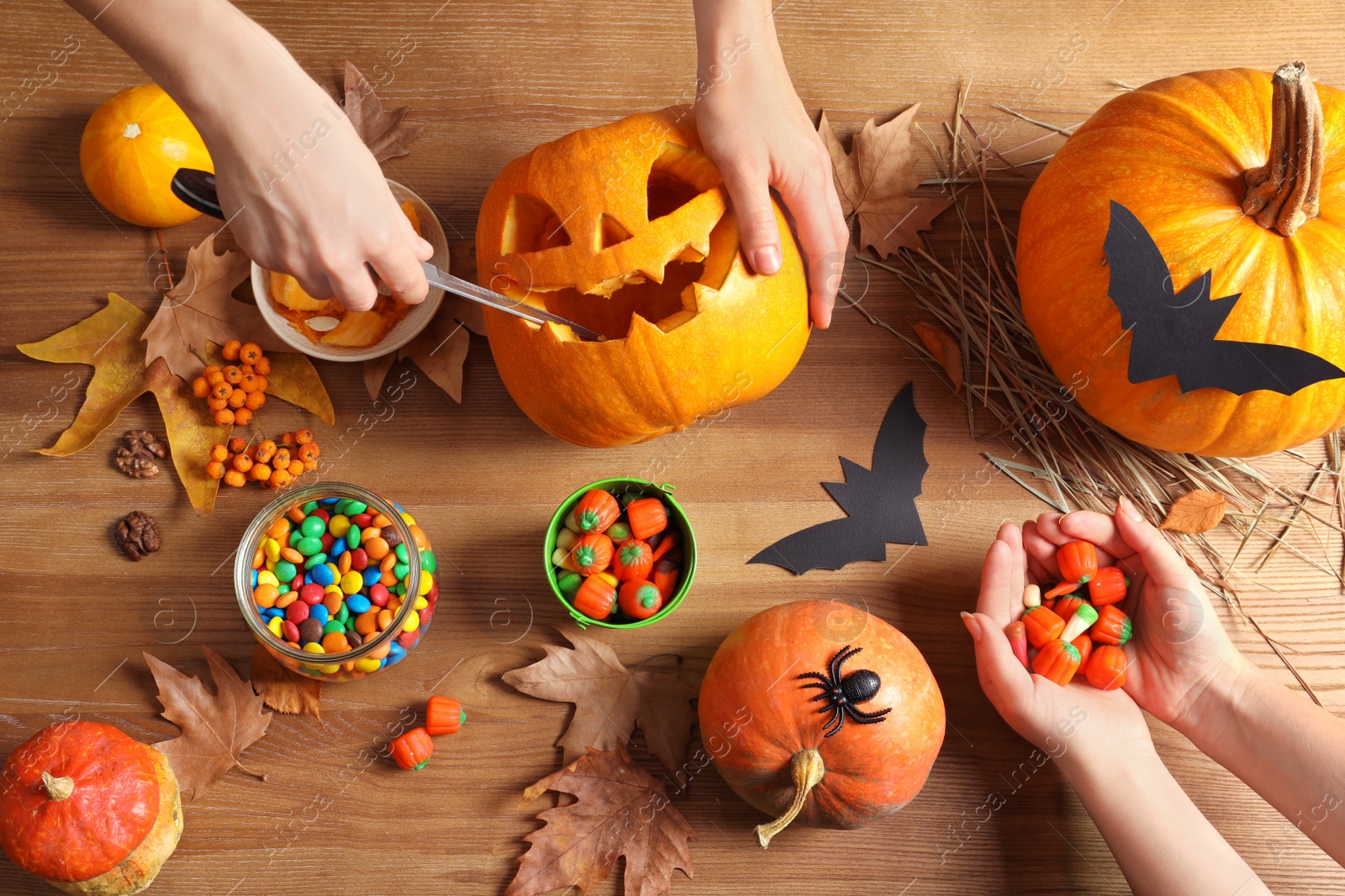 Photo of Women preparing Halloween pumpkin head jack lantern and holiday decorations on wooden table, flat lay composition